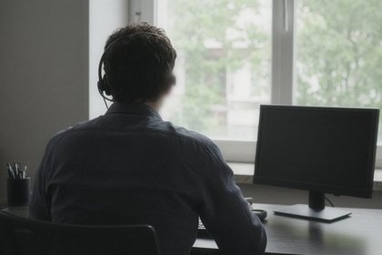 An office manager on a headset, seen from behind, at a desk by a bright window